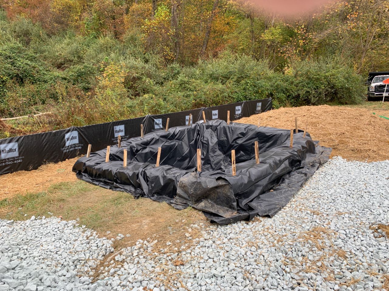 Black tarping over an erosion and sediment control element in a grassy area with gravel.