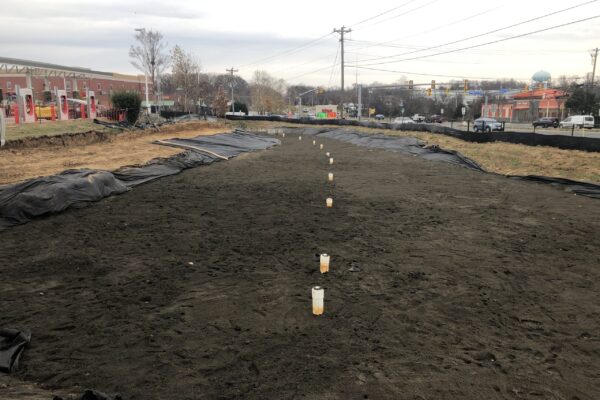 Green infrastructure jobsite near a gas station with PVC piping coming through the dirt