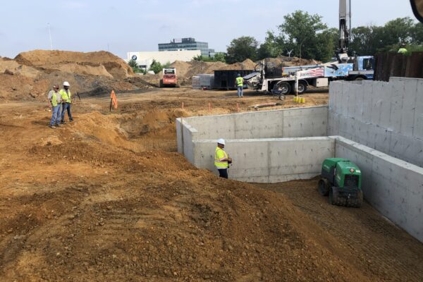 Multiple workers on a jobsite compacting soil outside of concrete structures.