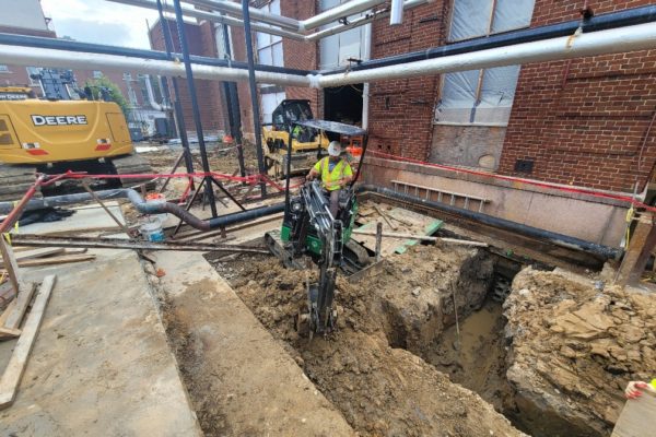 Operator using machinery outside of a building to dig a trench.