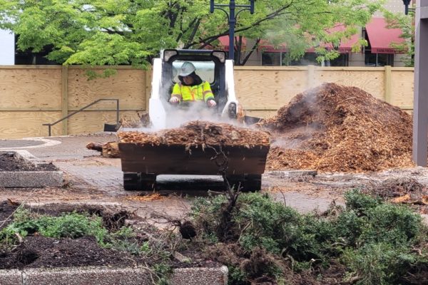 An operator using machinery to carry site debris across the jobsite in an urban area.