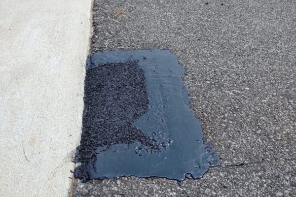 A section of replaced asphalt on the road near the sidewalk.