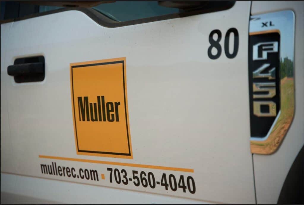 Close-up of a Muller-branded F-450 work truck displaying the company logo, website URL, and contact phone number, part of the Muller utility fleet.