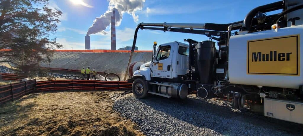 Workers in the background of a job site in a pit with a Muller truck in front of them and smoke stacks behind them.
