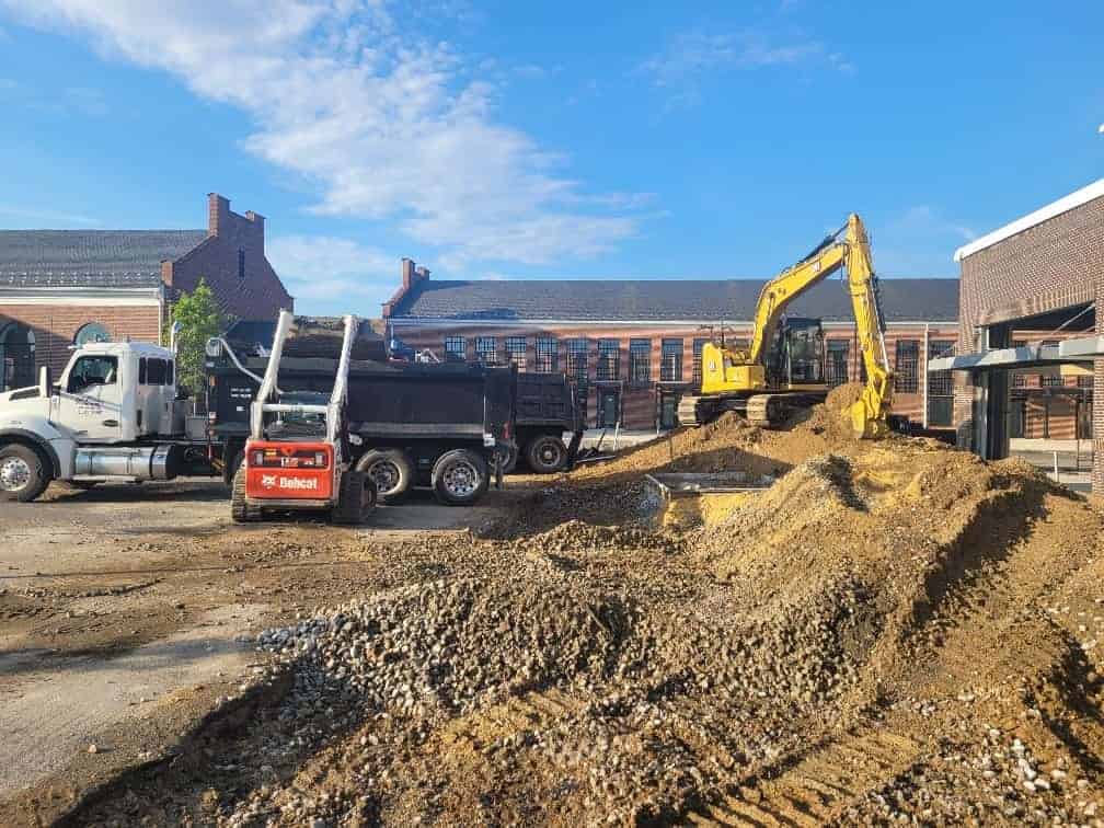 A skid steer and excavator work together to load material on to a dump truck as part of a site development project.