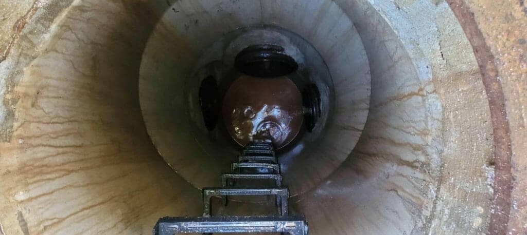 A downward shot into a man hole with a ladder leading down to an inspected storm drain.
