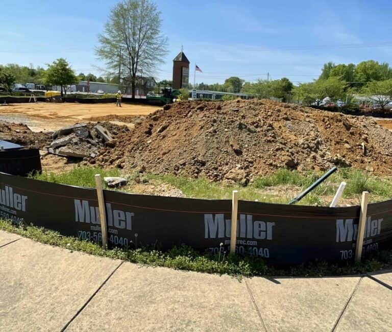 A perimeter control device with the Muller logo on it, on a job site with dirt and sediment piled up, used to prevent sediment pollution.