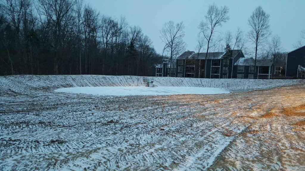 A snowy green infrastructure stormwater facility in a suburban neighborhood development near the woods.