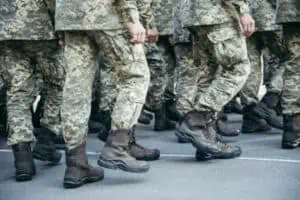 Soldiers in camouflage uniforms and black combat boots walking in formation on a paved road.