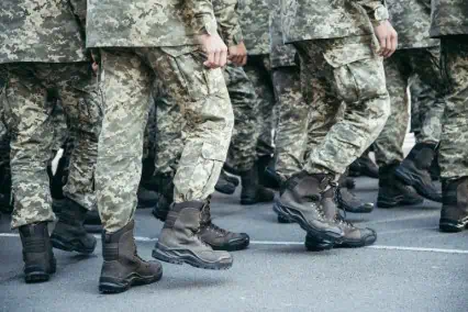 Soldiers in camouflage uniforms and black combat boots walking in formation on a paved road.