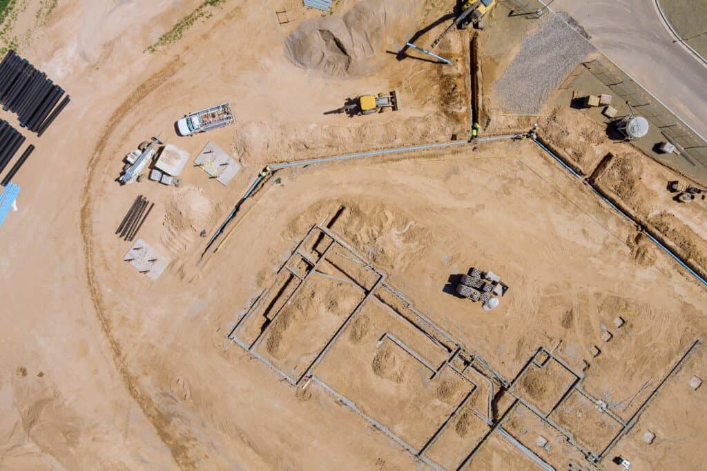 Aerial view of an active construction site showing utility installation, pipe staging, and earthmoving equipment during site development