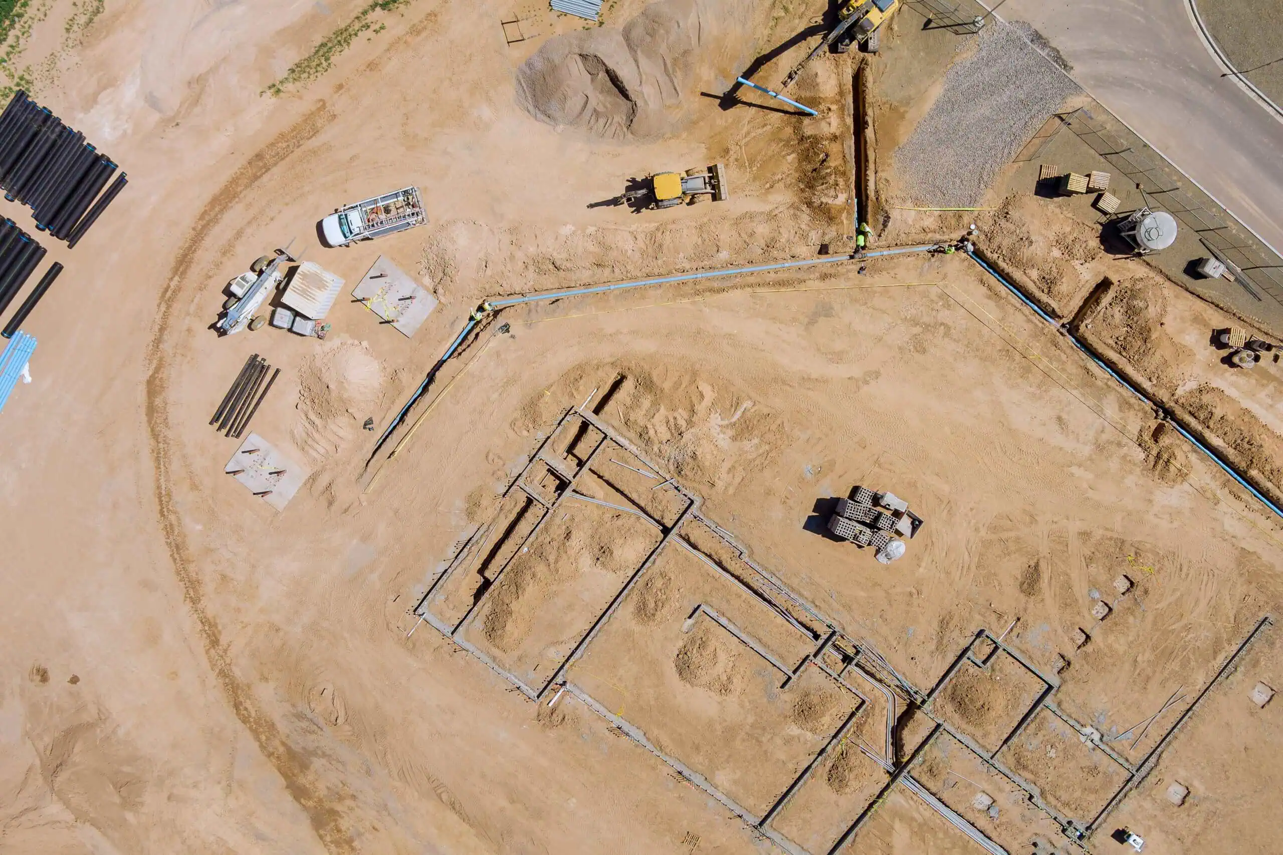 Aerial view of an active construction site showing utility installation, pipe staging, and earthmoving equipment during site development