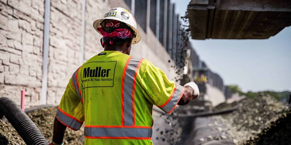 Up close shot of a crew member directing an operator where to place the gravel in a trench.